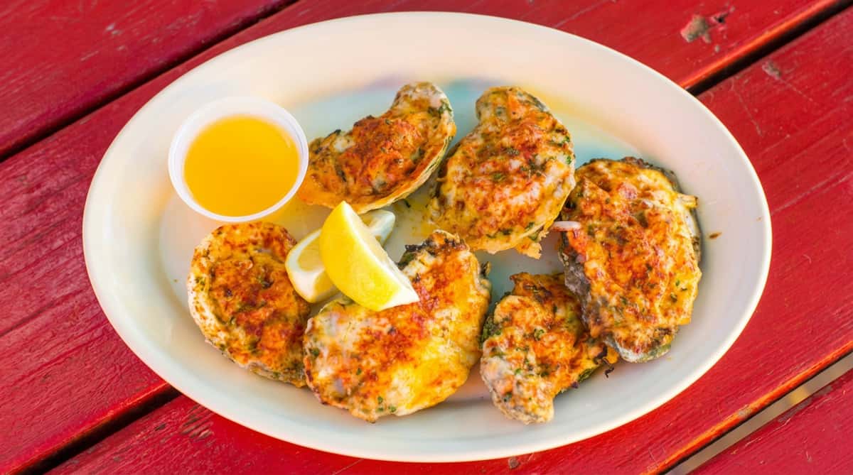 Baked oysters with cheese, herbs, lemon wedges, and a side of butter on a white plate.