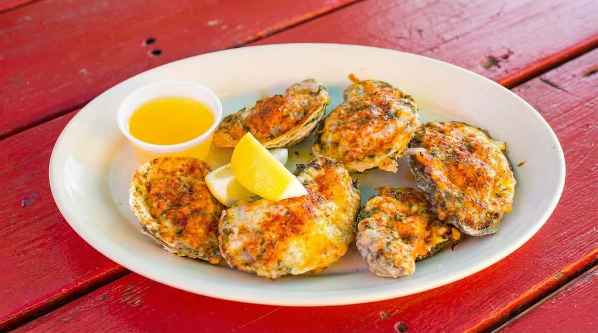 Baked oysters with cheese, herbs, lemon wedges, and a side of butter on a white plate.