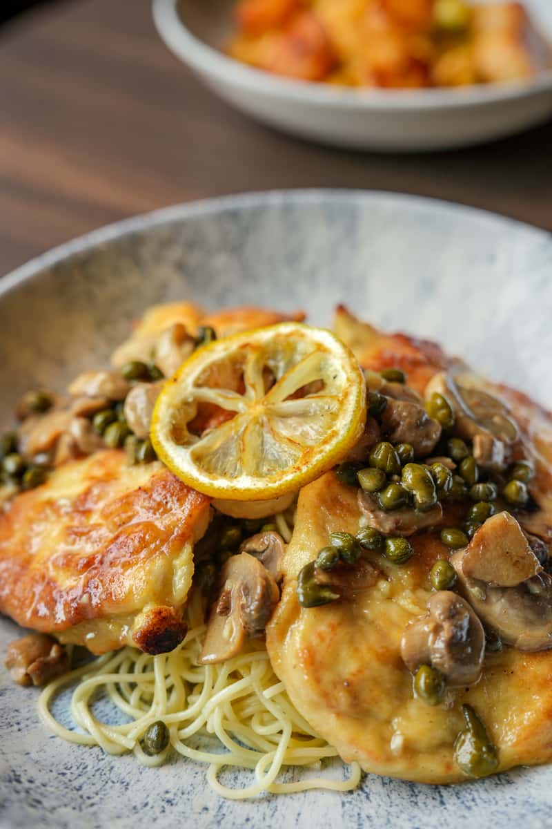 Welly's golden Chicken Piccata with capers, sautéed mushrooms, and a roasted lemon slice served over pasta.