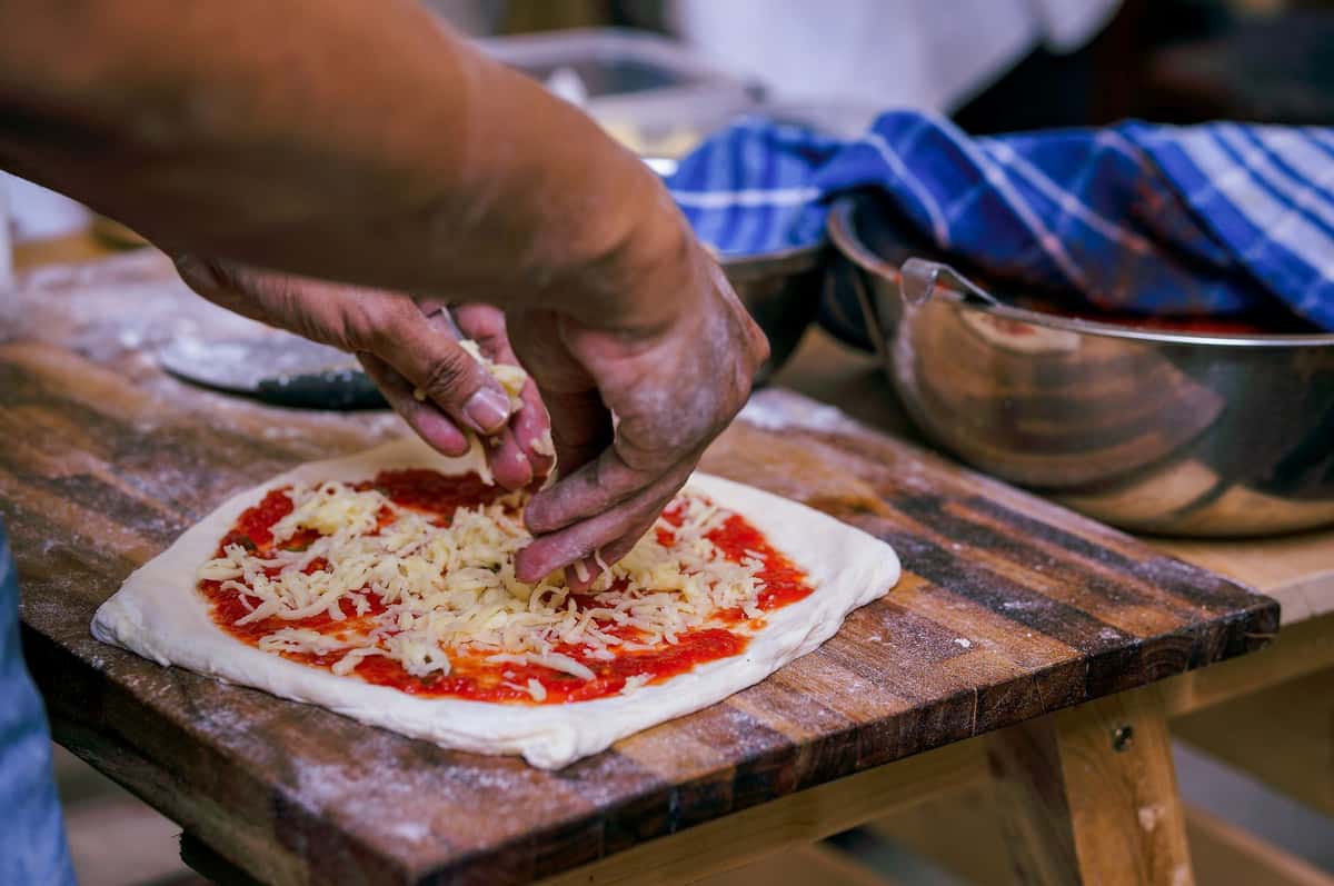 Close-up of a person adding cheese to a homemade pizza on a wooden board.