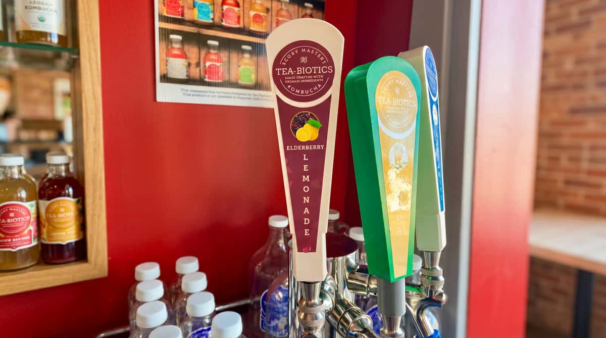 White kombucha tap handle for Elderberry Lemonade, with two other tap handles and bottles in the background.