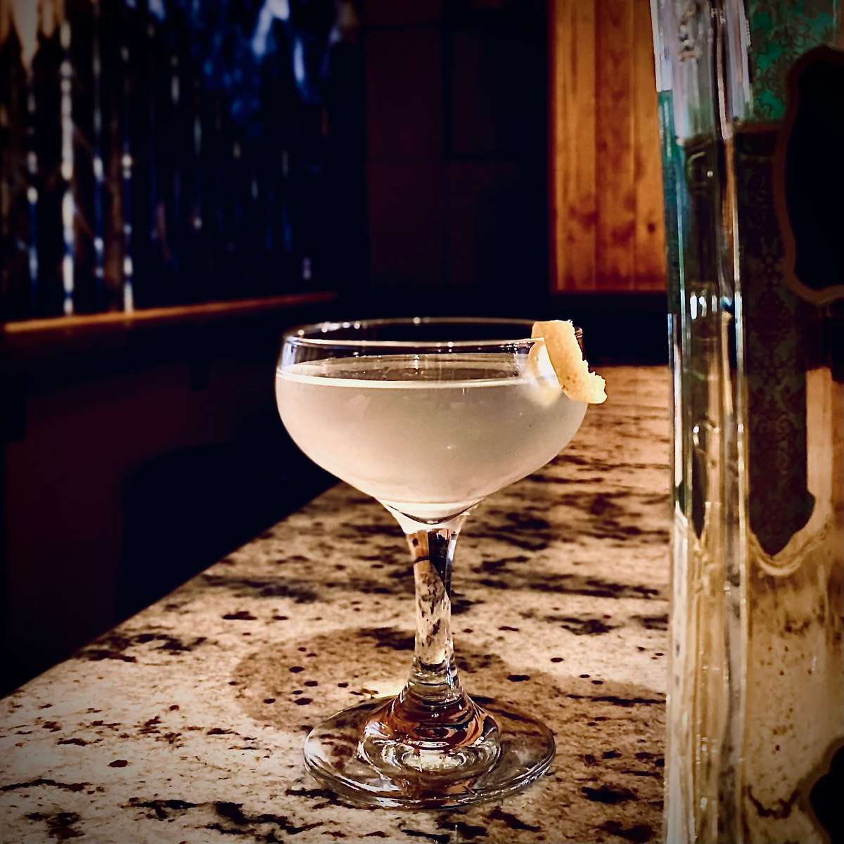 Image Description: A clear beverage in a coupe glass is garnished with a lemon twist.