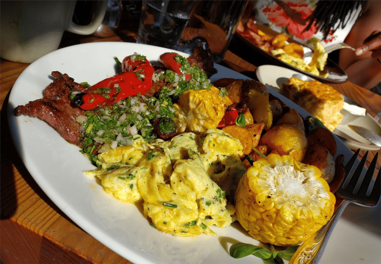 breakfast platter with scrambled eggs, potatoes, bacon, corn, and peppers