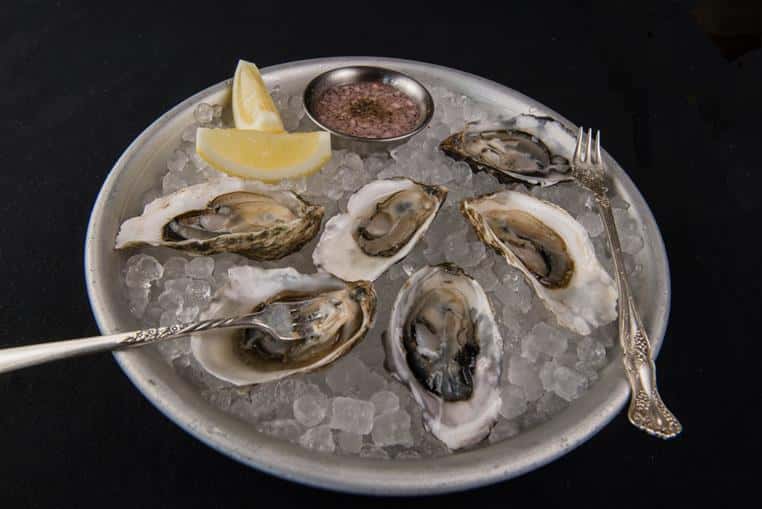raw oysters on ice with side of dipping sauce and lemon wedges