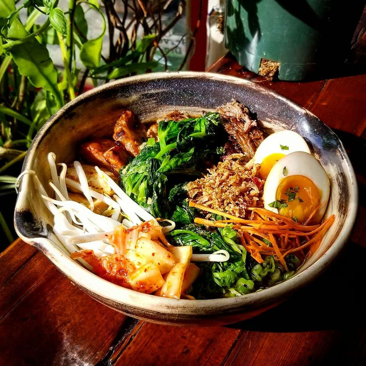 An image of Pinwheel Garden's short rib rice bowl containing kimchi, snow pea leaves, a marinated egg, and assorted garnishes