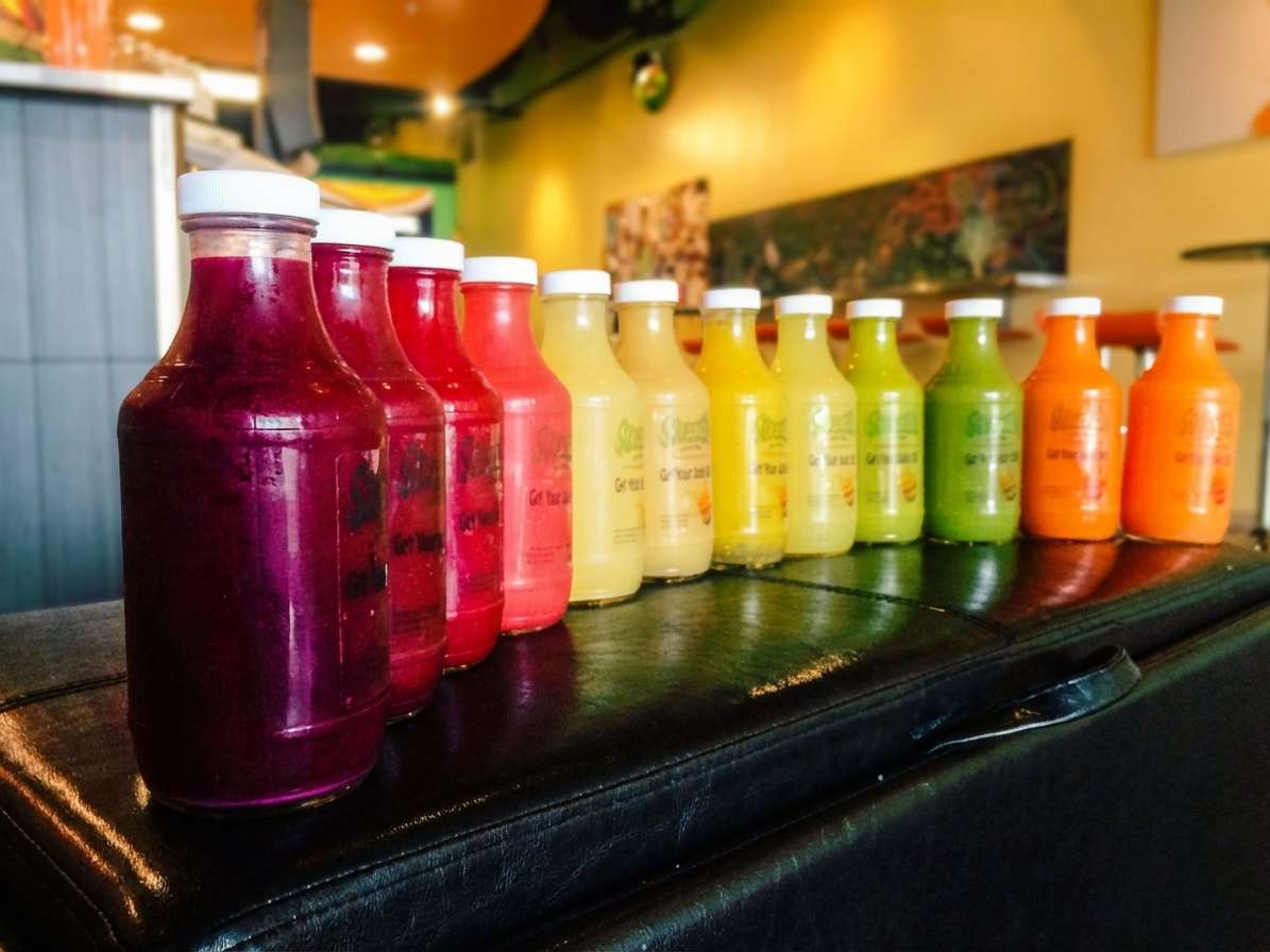 Assorted cold-pressed juices in vibrant rainbow colors lined up on a counter, showcasing a variety of fruit and vegetable blends