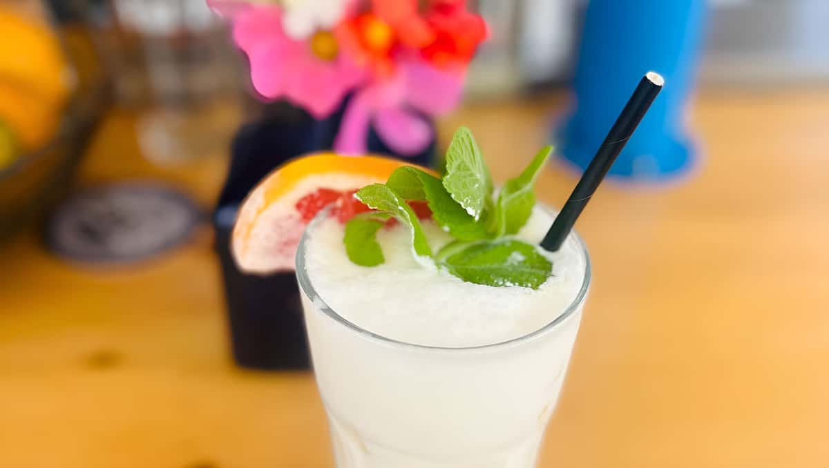 A glass filled with a white frozen slushy drink, garnished with fresh mint and a slice of pink grapefruit.