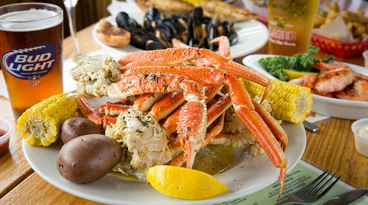 Plate of steamed crab legs, corn on the cob, potatoes, and a lemon wedge.