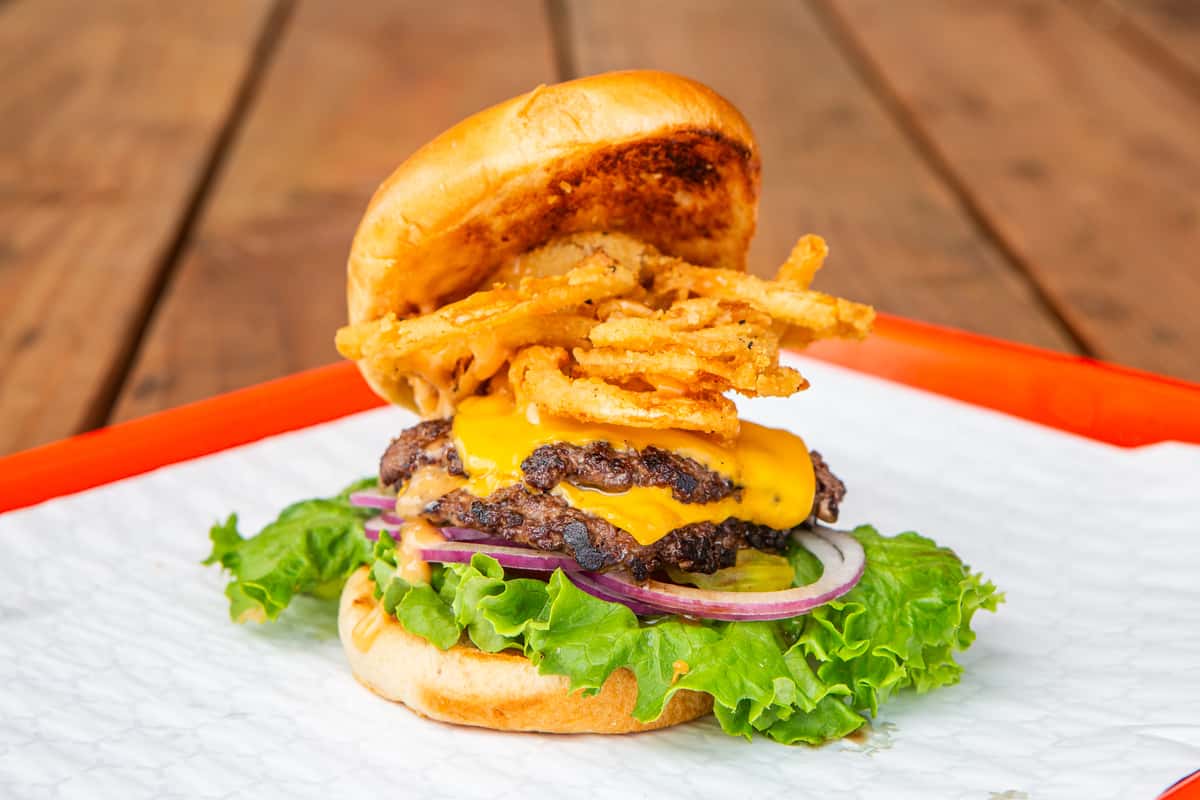 Jimmy's burger stacked with cheese, crispy onion rings, lettuce, tomato, and onion in Hurst, TX
