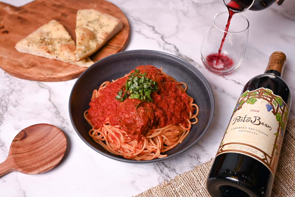 Picture of a plate of pasta next to a bottle of wine.