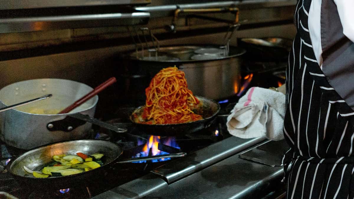 chef flipping a pan of spaghetti over open flame.