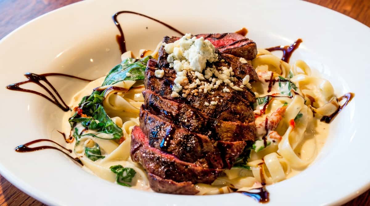 Seared steak medallions over creamy fettuccine Alfredo with spinach and balsamic drizzle, a signature steak and pasta entrée at Tanino Ristorante Italiano.