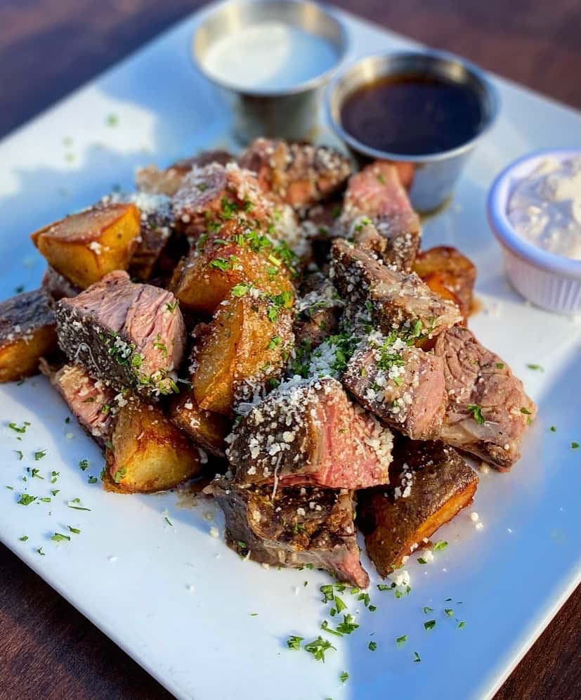 Cubed meat meal, seasoned and covered with garnish served with sauces