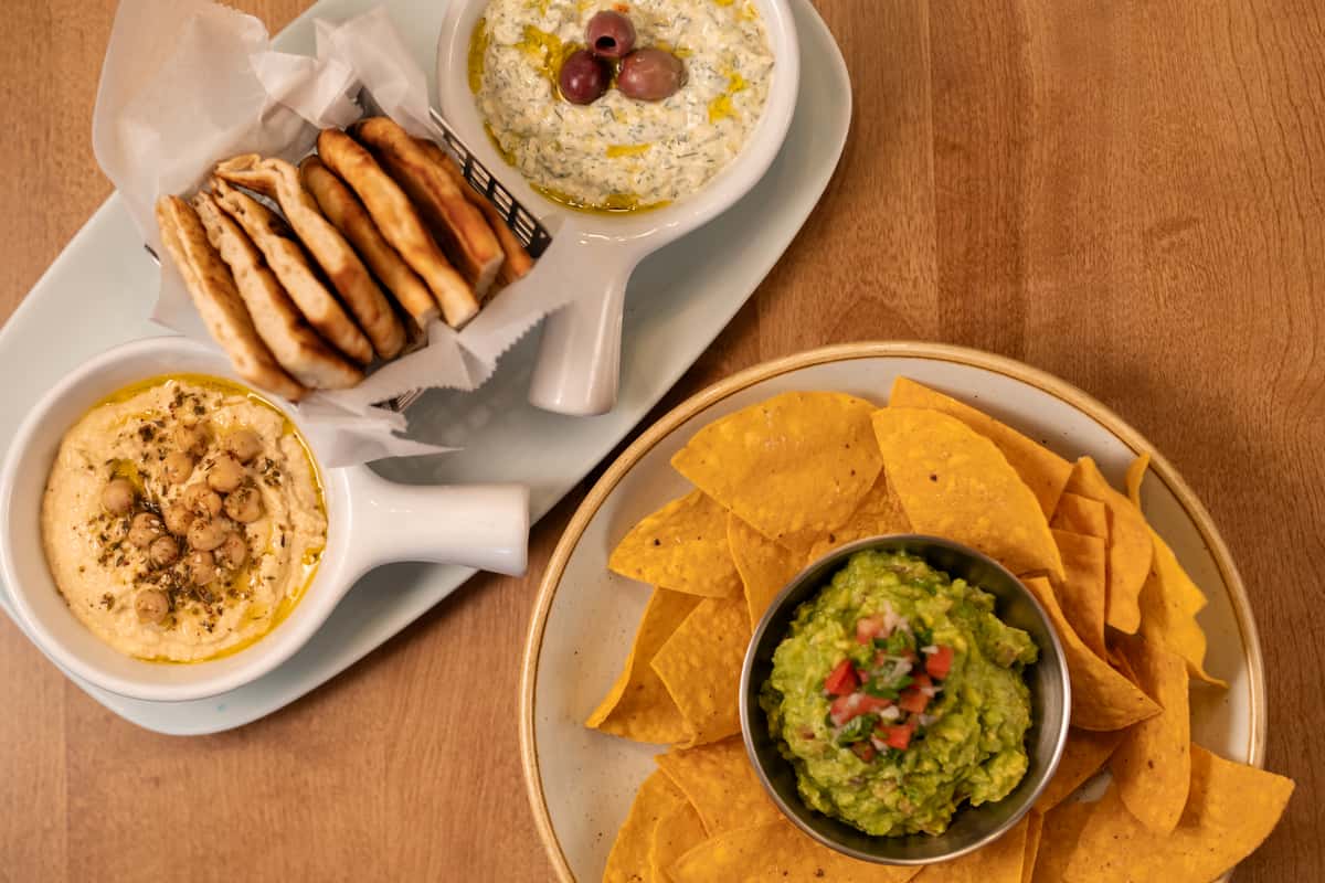 Hummus and pita beside a plate with guacamole and tortilla chips