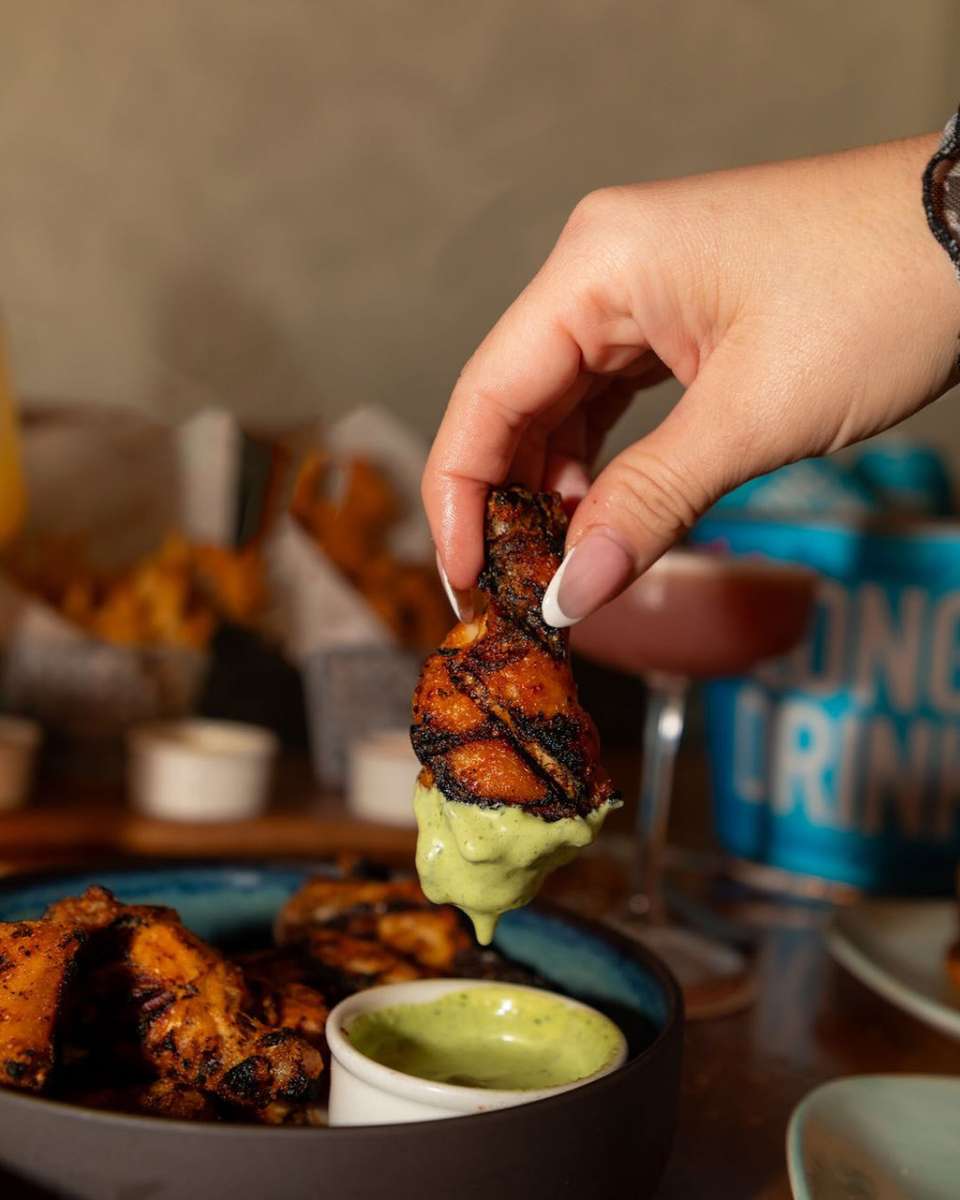 Woman's hand dipping grilled chicken into a green sauce