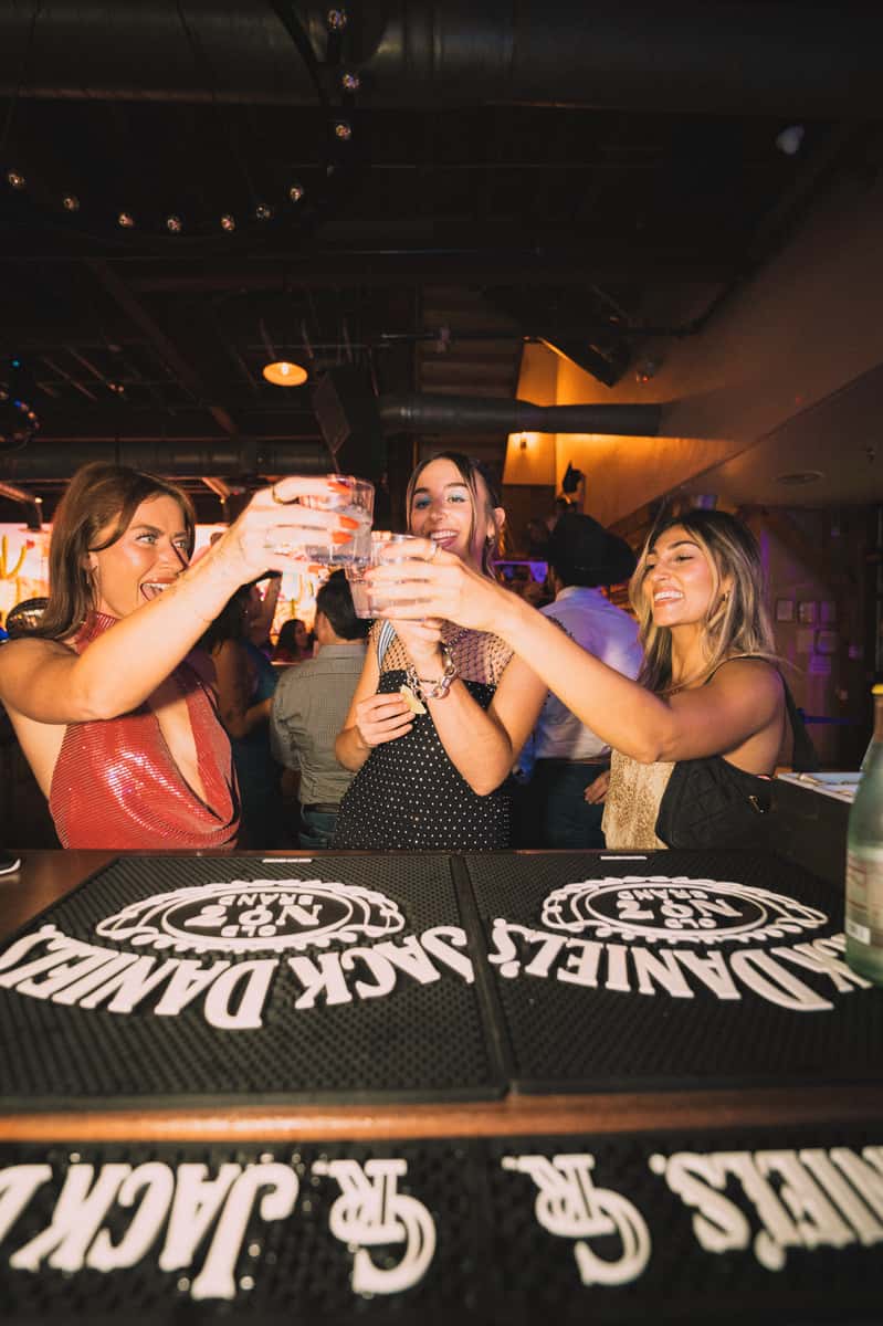 Guests toasting drinks at the bar in a high-energy country nightlife venue with a social party atmosphere.