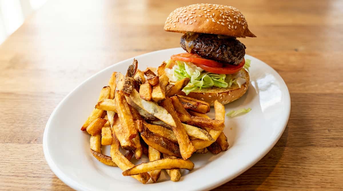 Cheeseburger with lettuce, tomato, and a side of french fries on a white plate.