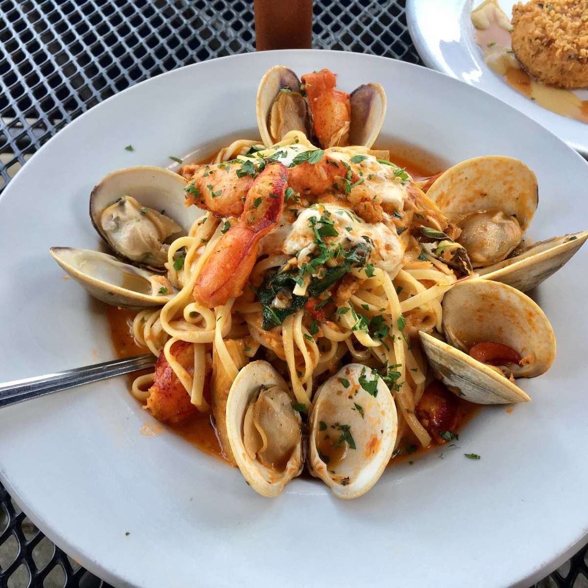 A vibrant seafood pasta dish is beautifully presented, featuring tender clams in their shells tossed with spaghetti in a rich, savory tomato sauce. The pasta is garnished with fresh herbs and a sprinkle of cheese, adding color and depth. Set on a clean white plate, the dish looks fresh, flavorful, and perfectly suited for a coastal dining experience.