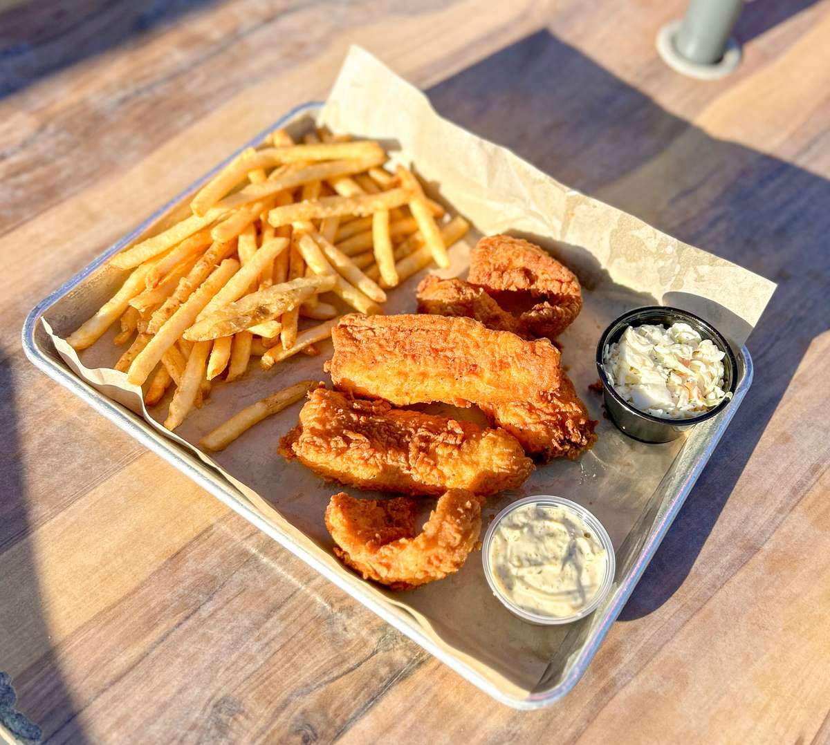 Crispy golden-fried catfish filets served with seasoned fries, tartar sauce, and creamy coleslaw on a tray—classic Southern fish fry served al fresco.
