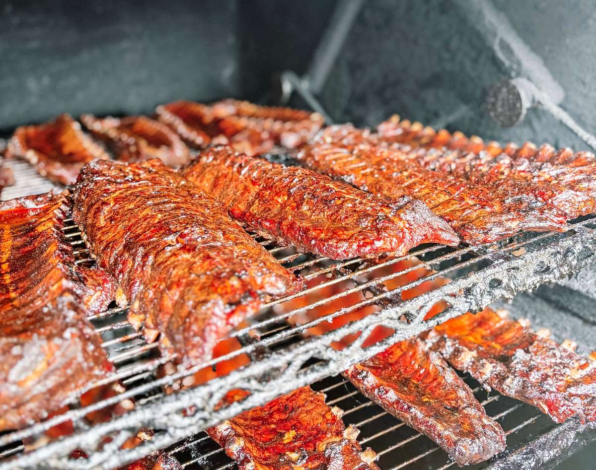 Close-up of juicy, slow-smoked pork ribs on a multi-level smoker, glistening with a caramelized BBQ glaze—classic Southern barbecue in the making.