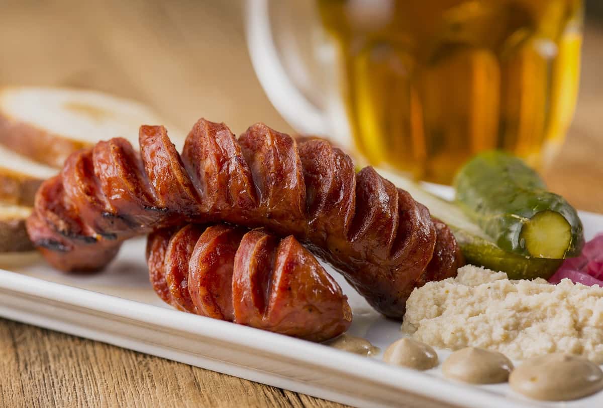 Sliced sausages plated with a side of mash and pickles, served with a drink