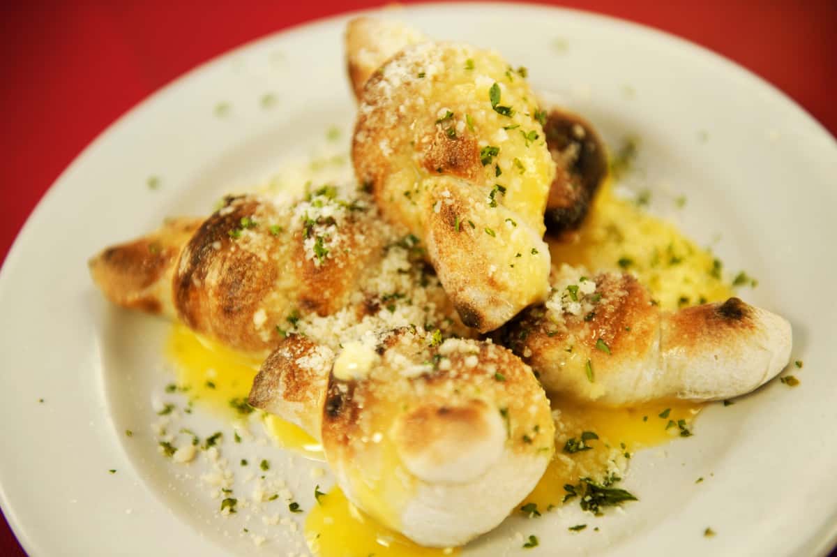A plate of golden-brown dough knots generously coated in garlic butter, oil, and herbs.