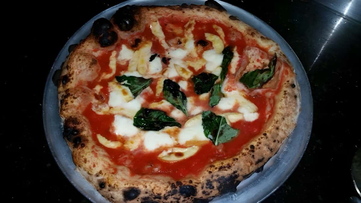 A top-down view of a rustic, round pizza featuring red sauce, melted fresh mozzarella patches, and basil leaves.