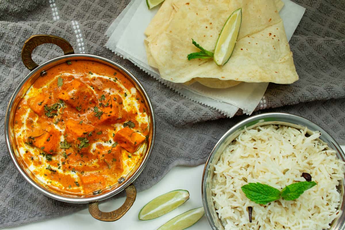 Creamy paneer butter masala with basmati rice and folded naan, styled in an elegant Indian restaurant flat lay.
