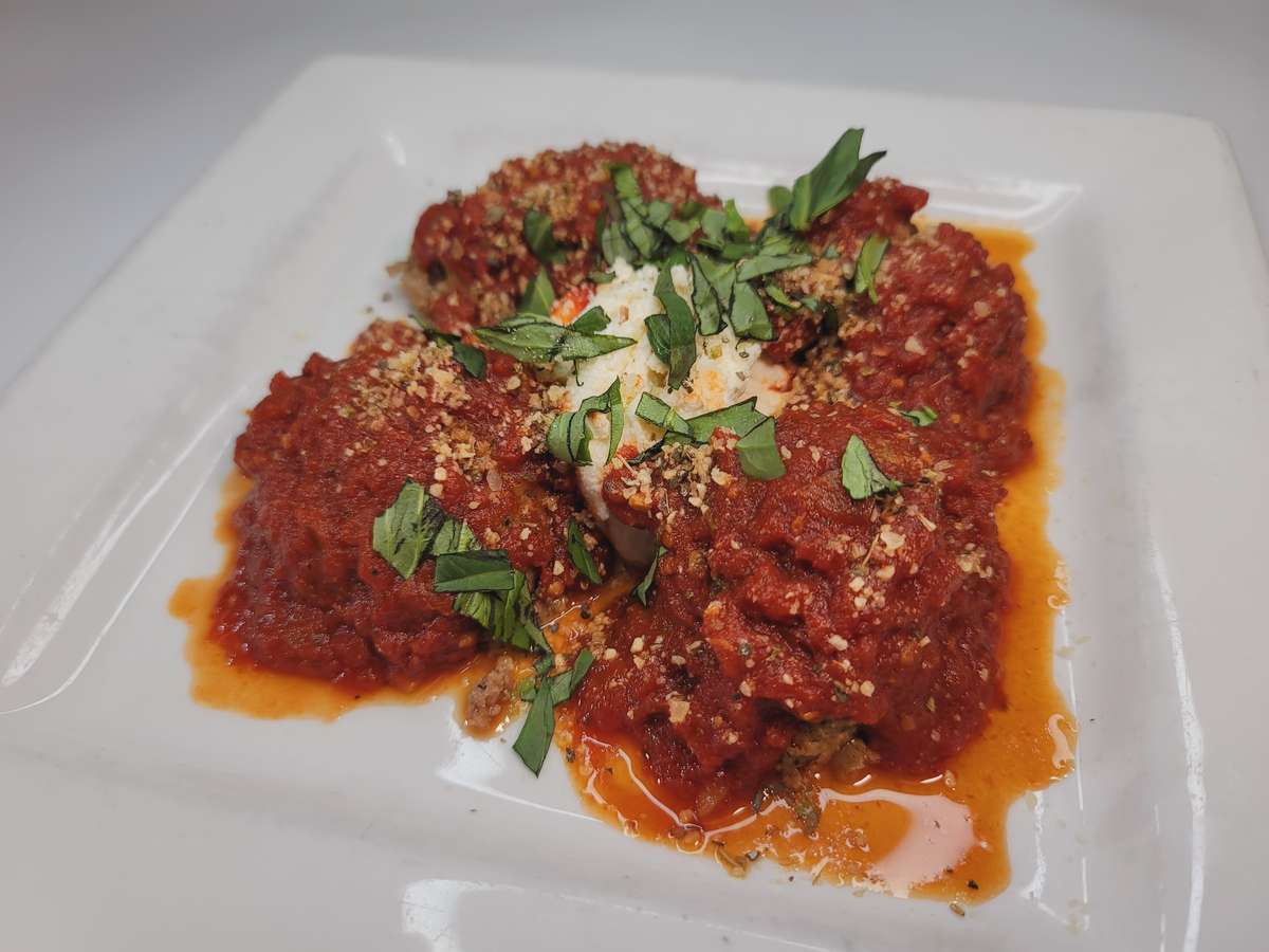 Meatballs in rich red sauce topped with cheese, basil, and breadcrumbs on a white plate from Gasparilla.