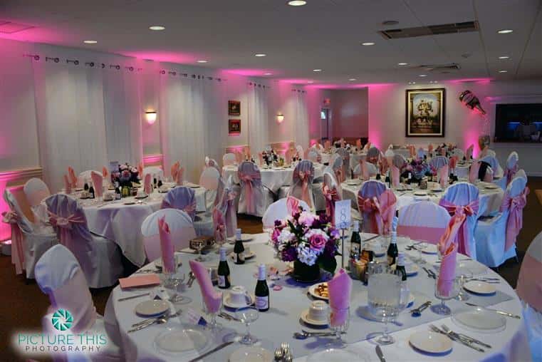 large banquet room with several tables set up with plates and silverware with a bouquet in the middle