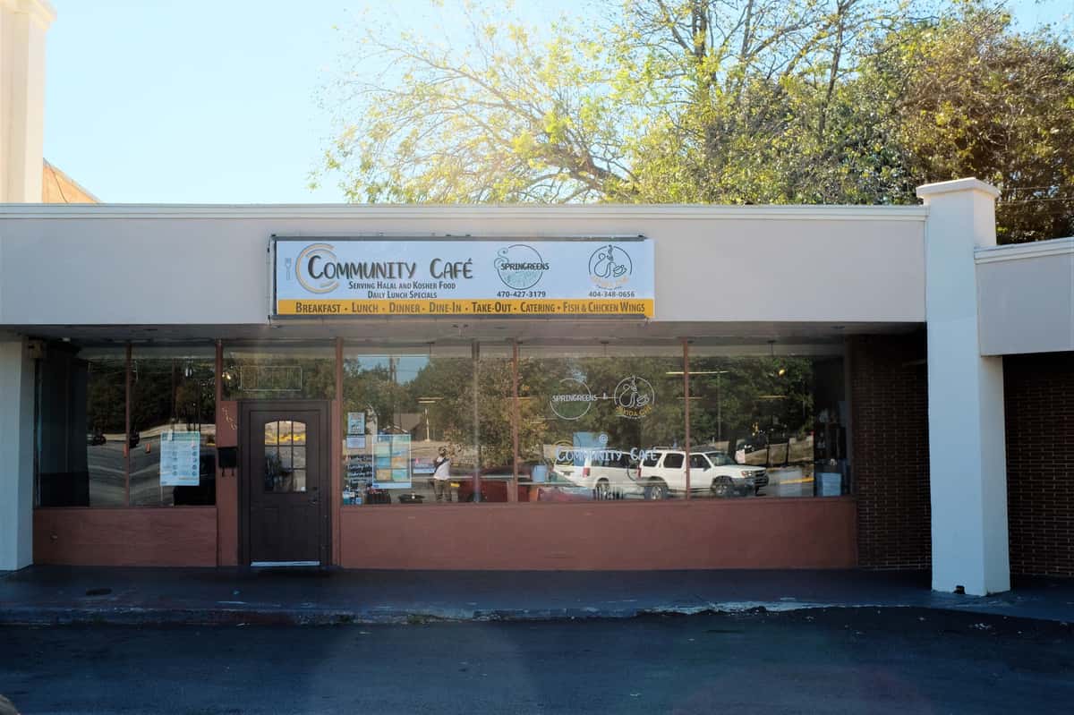 Exterior of Community Café, a casual dining spot serving halal and kosher food with breakfast, lunch, dinner, and catering options, featuring a large glass storefront and signage promoting fish and chicken wings.