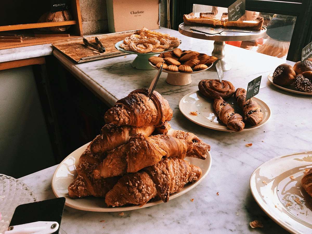 A display of freshly baked croissants, pastries, and desserts on a marble countertop, with price tags for each item.
