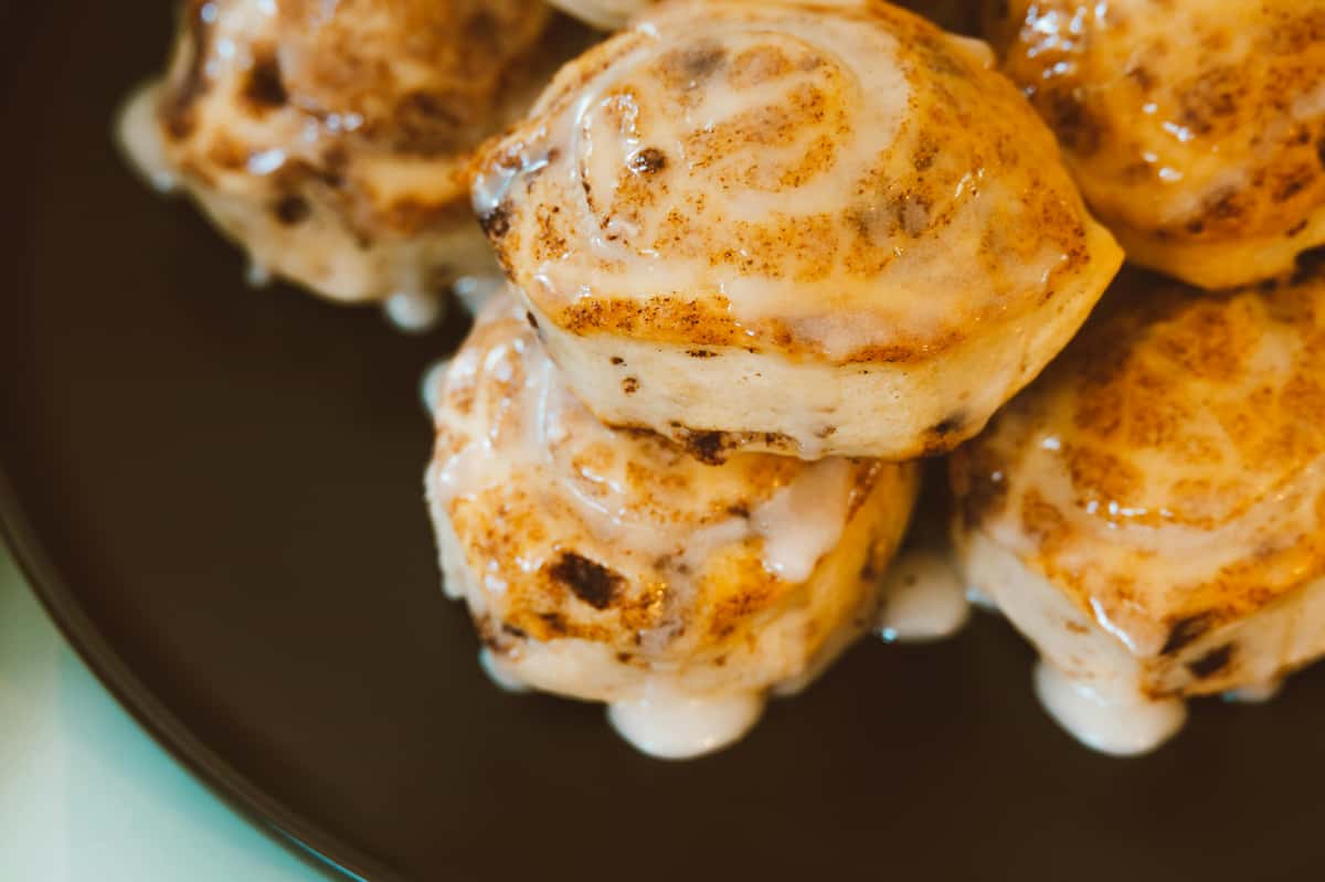 Cinnamon rolls with a glaze on top, stacked neatly on a dark plate, showcasing their sweet and indulgent layers.
