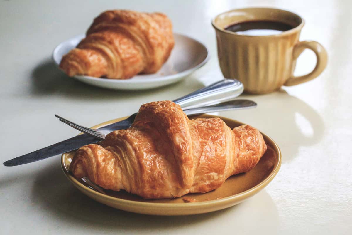 A freshly baked croissant on a plate, paired with a cup of coffee, ready for a perfect breakfast or snack.