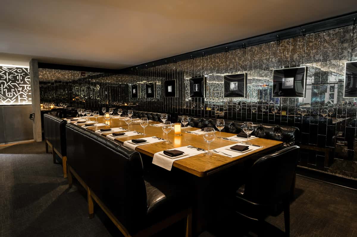 Chic Nashville steakhouse private dining space, with a long table, tufted leather banquettes, and walls adorned with ornate mirrors and black-and-white framed art.