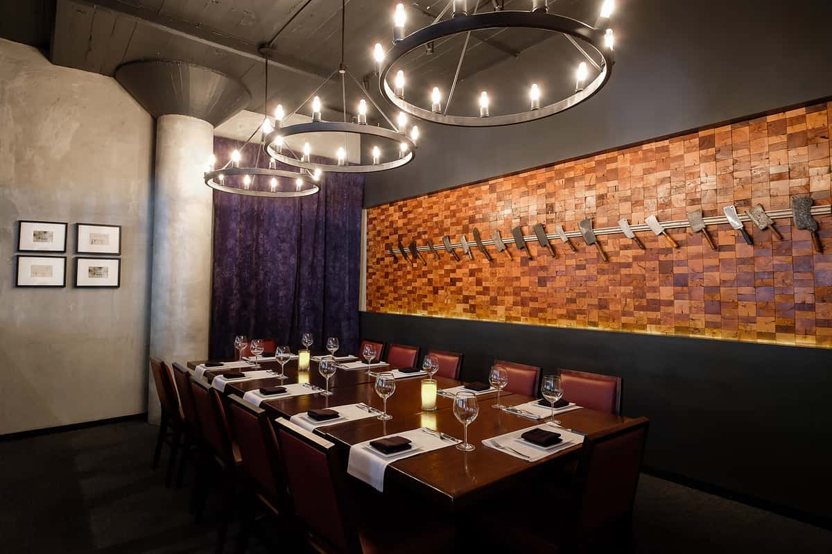 Sophisticated Nashville steakhouse private dining room with circular chandeliers, leather chairs, framed artwork, and a unique wooden block wall feature.