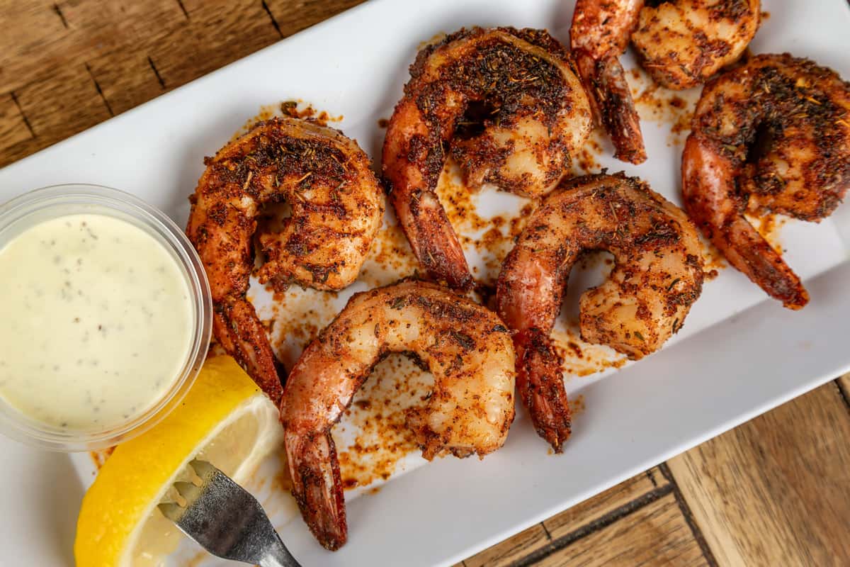 Blackened shrimp seasoned with herbs and spices, served with a lemon wedge and side of ranch dressing on a white plate.