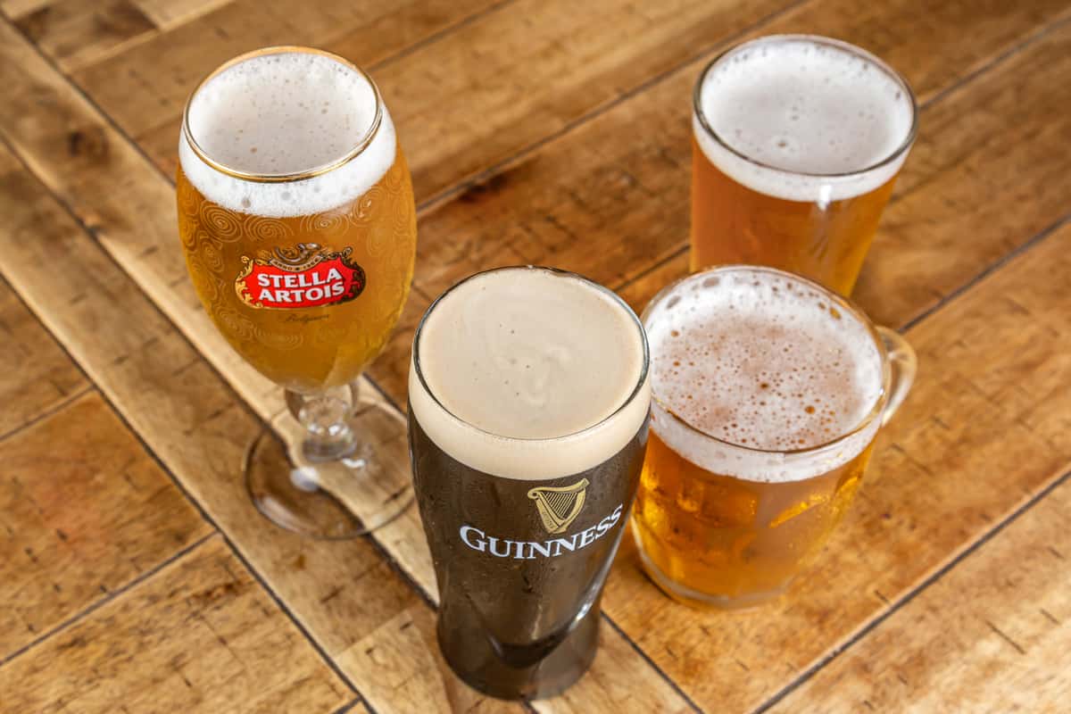 Four glasses of beer, including Stella Artois and Guinness, arranged on a wooden table.