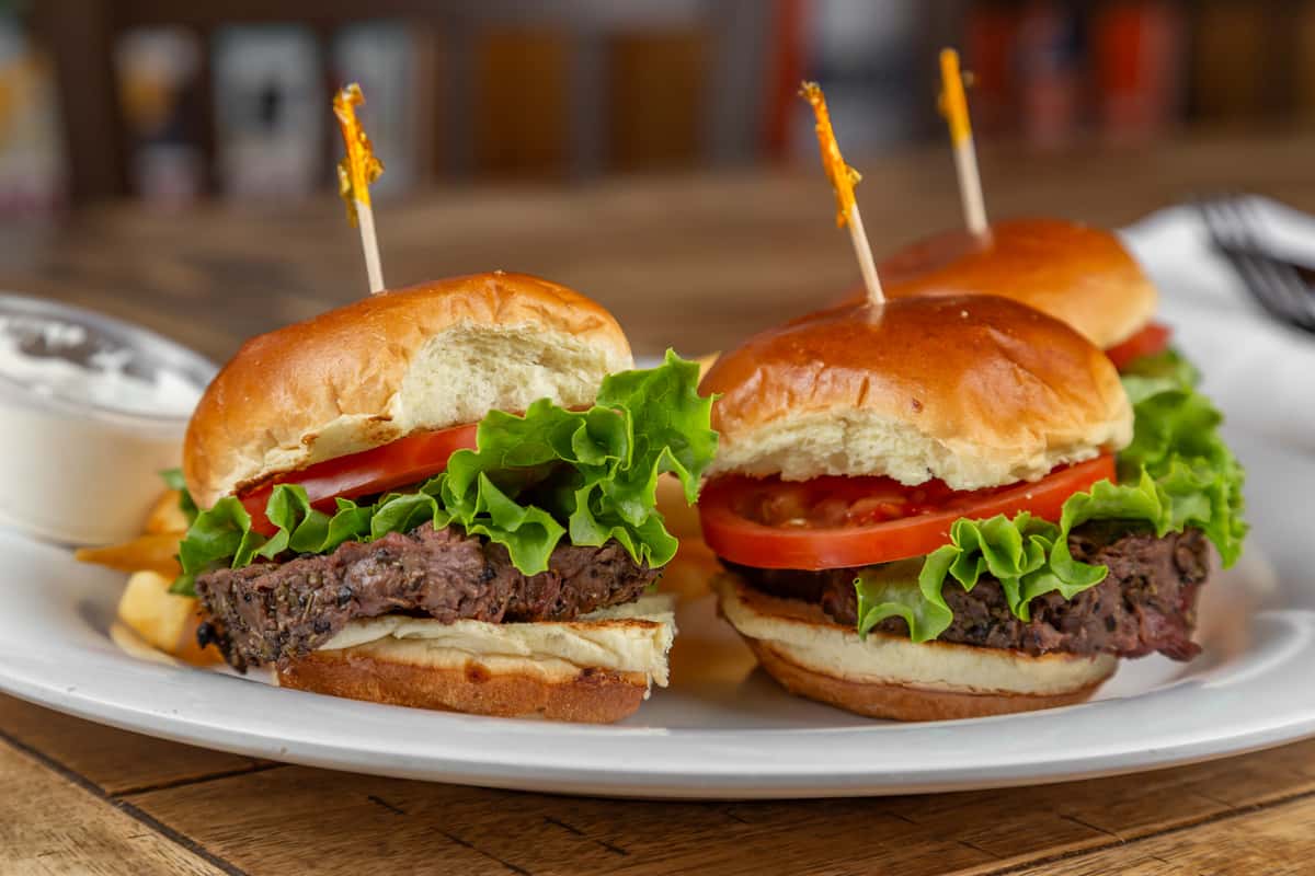 Three beef sliders with lettuce and tomato served with fries and a side of ranch dressing on a white plate.