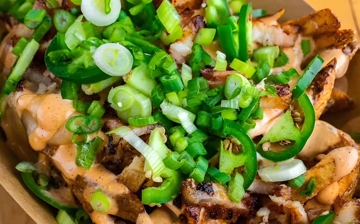 A dish topped with plenty of sliced green onions, peppers, and a creamy orange sauce.