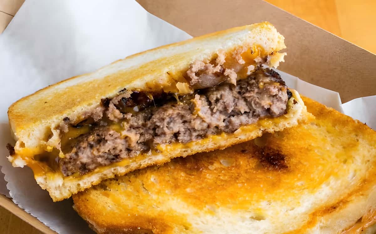 A toasted sandwich sliced in half, showing a beef patty and melted cheese inside