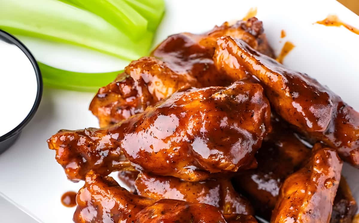 A close-up shot of chicken wings coated in a dark, glossy sauce with a side of celery and dipping sauce.