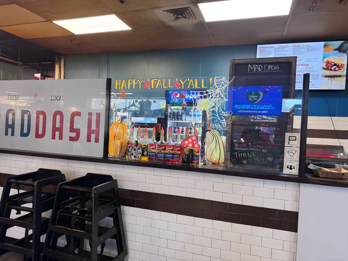 An interior shot of a restaurant's order counter with high chairs and menu displays in the background.