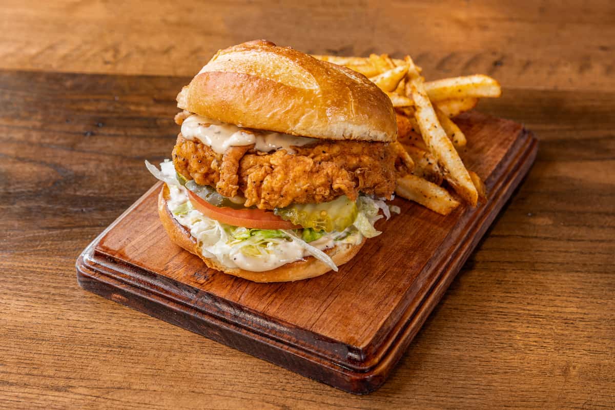 crispy fried chicken sandwich with lettuce and sauce served with seasoned fries on a rustic wooden board