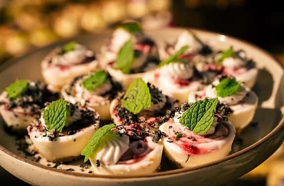 Mini white chocolate mousse cups with berry swirl, topped with fresh mint leaves and cookie crumble on a ceramic plate.
