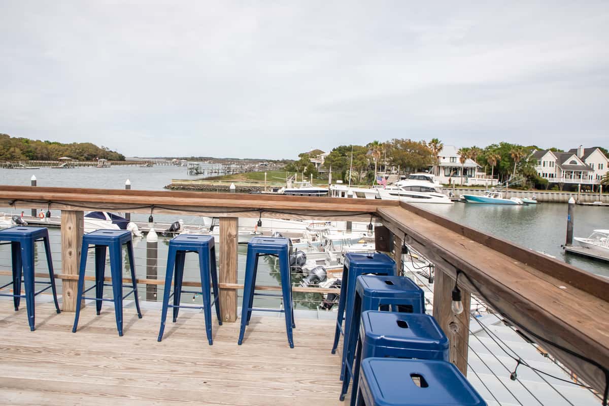waterfront outdoor bar deck with blue stools overlooking a marina and coastal homes