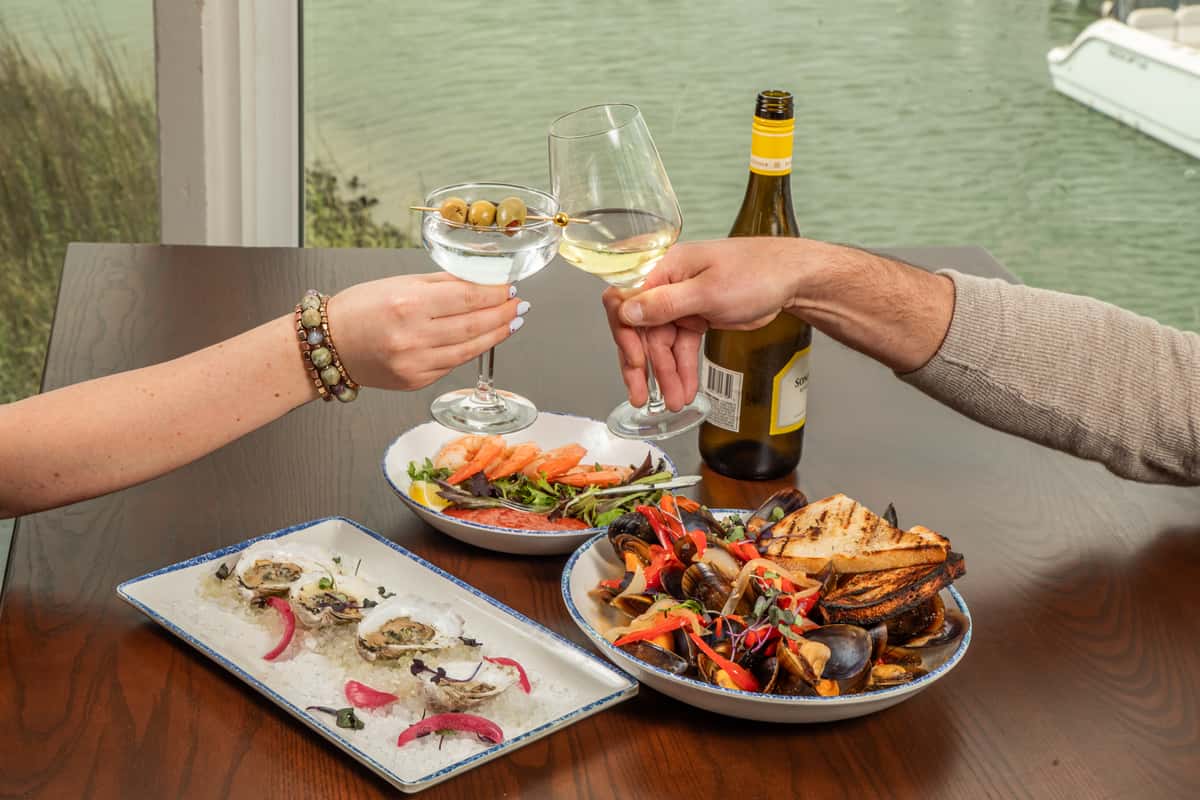 guests toasting drinks over a table with seafood dishes in a coastal restaurant