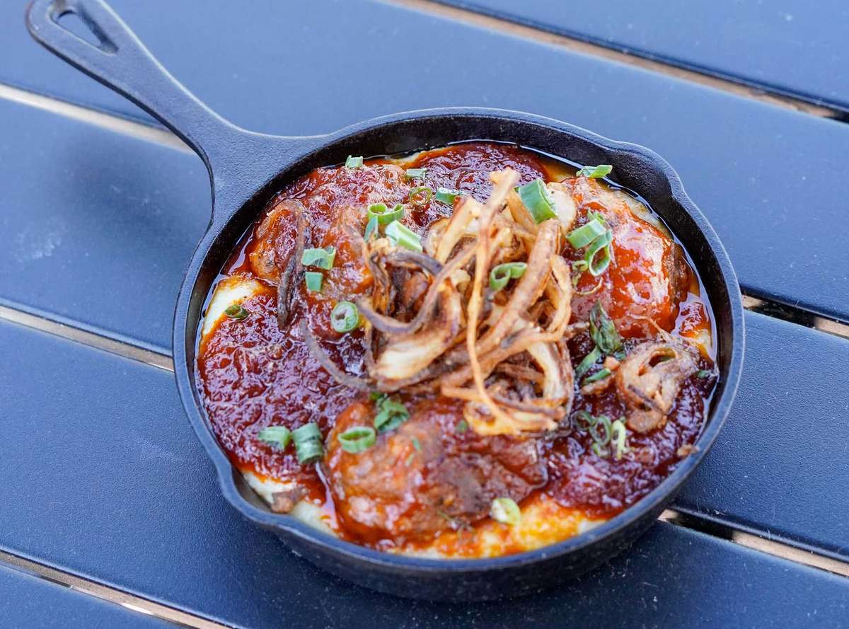 Cast iron skillet meatballs topped with rich marinara sauce, crispy fried onions, and green onions over creamy polenta