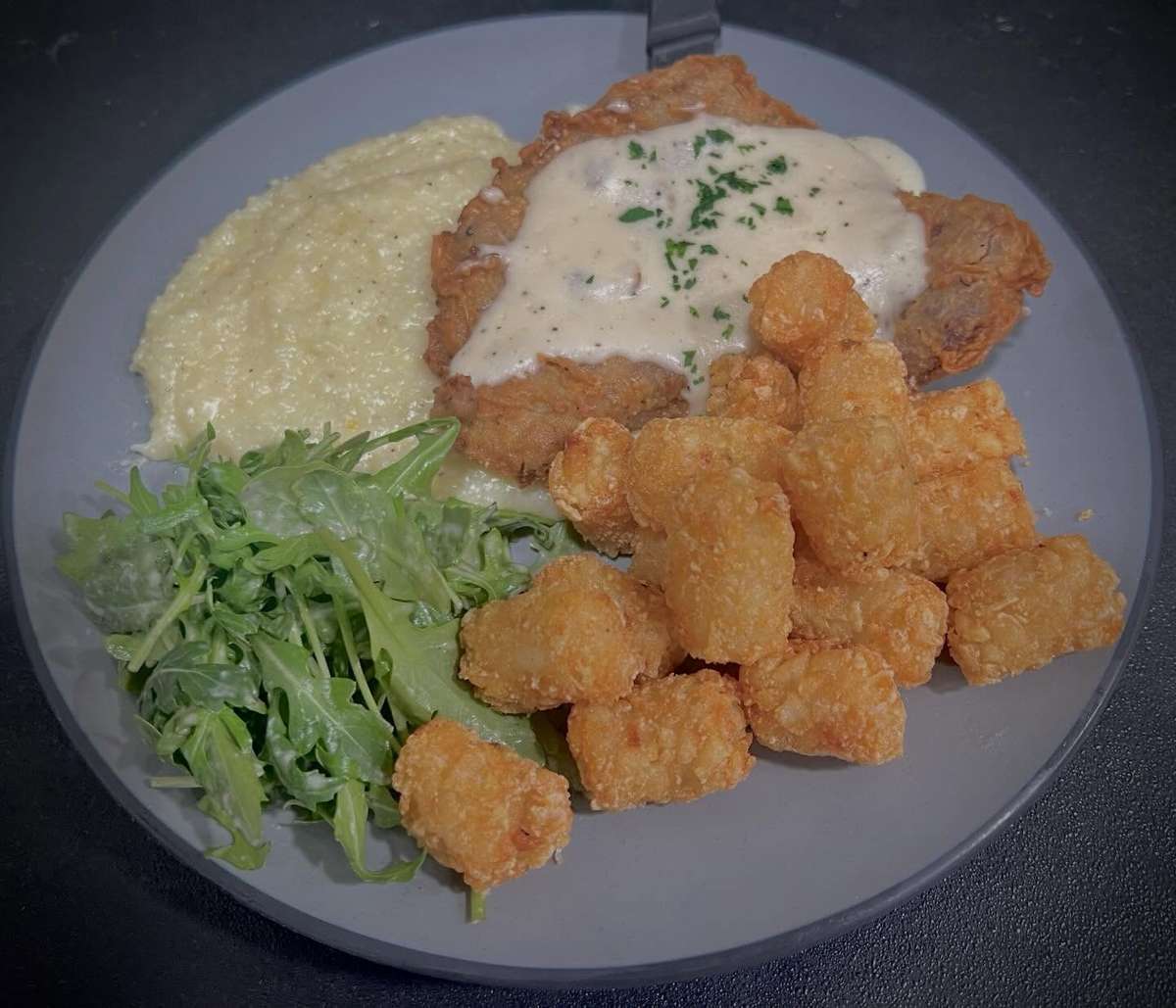Southern fried chicken plate with creamy grits, crispy tater tots, white gravy, and fresh arugula salad