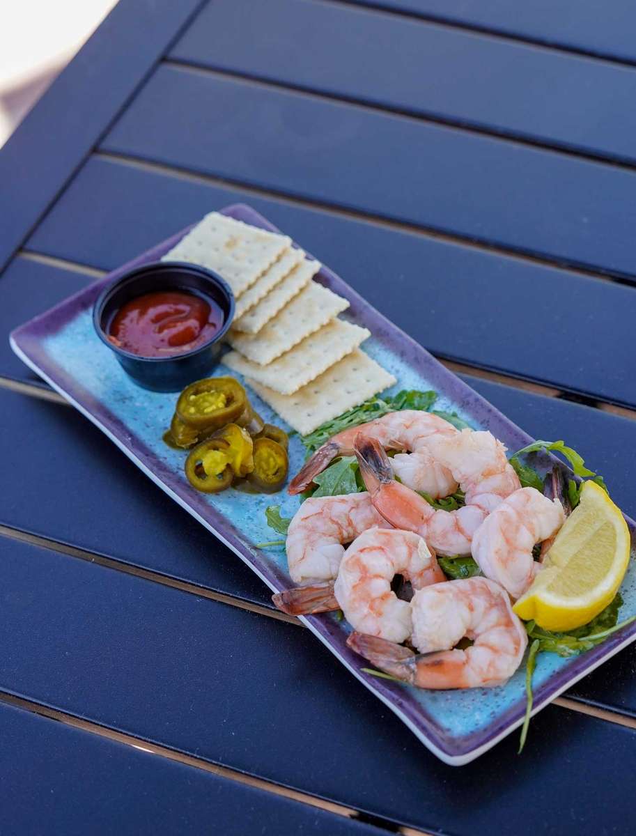 Chilled shrimp cocktail platter with lemon wedge, crackers, jalapeños, and cocktail sauce served on a modern seafood appetizer plate